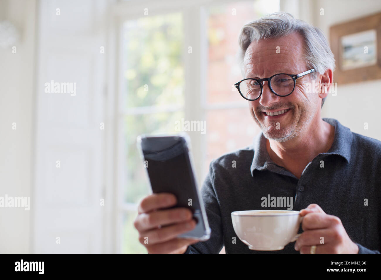 Smiling mature man drinking tea and using smart phone Stock Photo