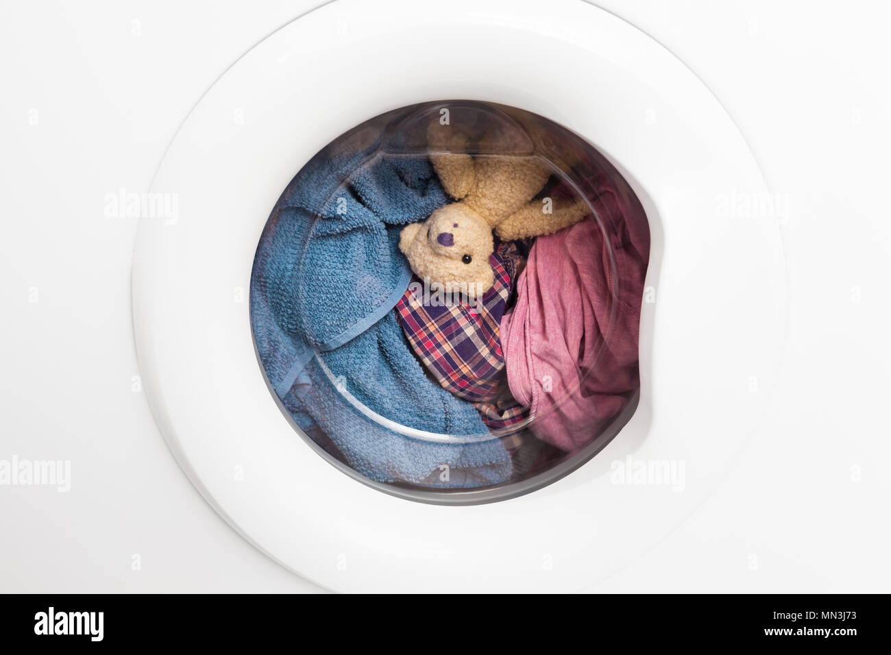 Window door of washing machine with laundry and toy teddy bear inside who takes a look out (copy space) Stock Photo