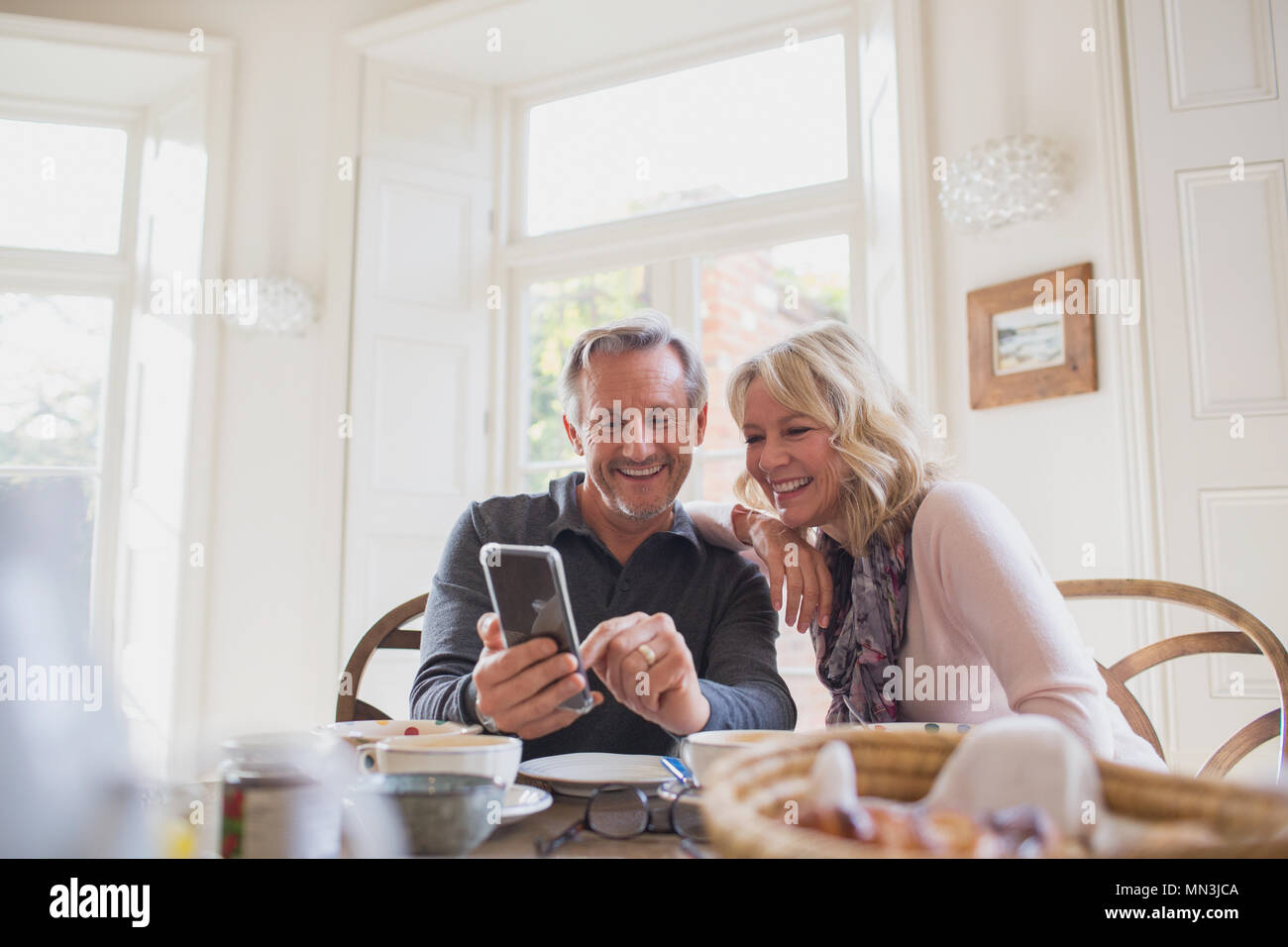 Smiling mature couple using smart phone at dining table Stock Photo