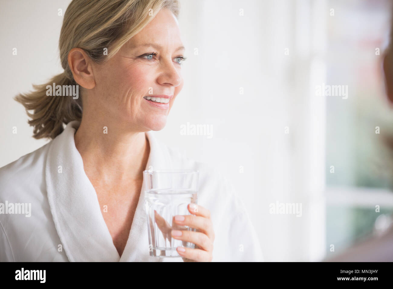 Smiling mature woman in bathrobe drinking water Stock Photo Alamy