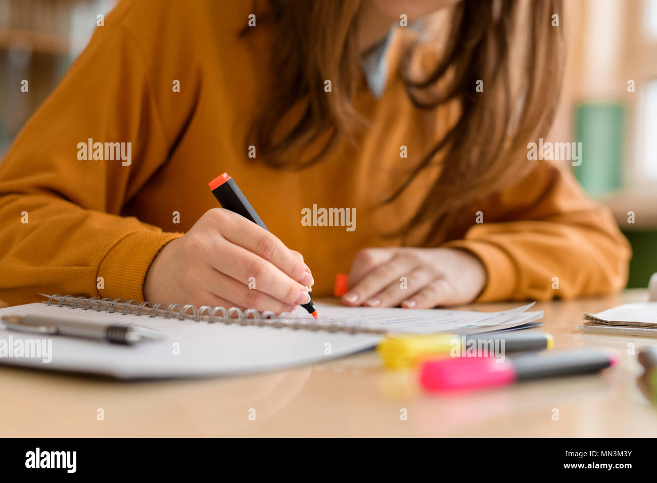 Young unrecognisable female college student in class, taking notes and using highlighter. Focused student in classroom. Authentic Education concept. Stock Photo