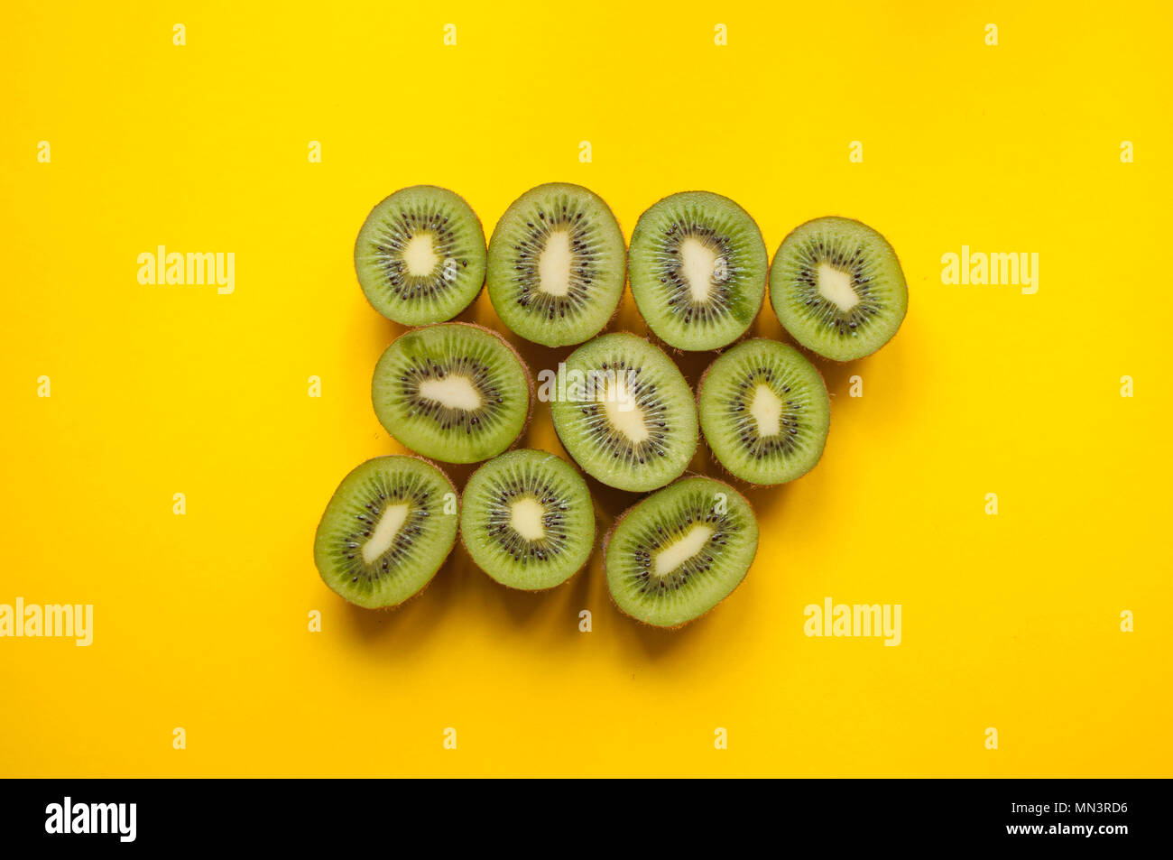 Flat lay of many halves of green kiwi fruit on bright yellow background. Stock Photo