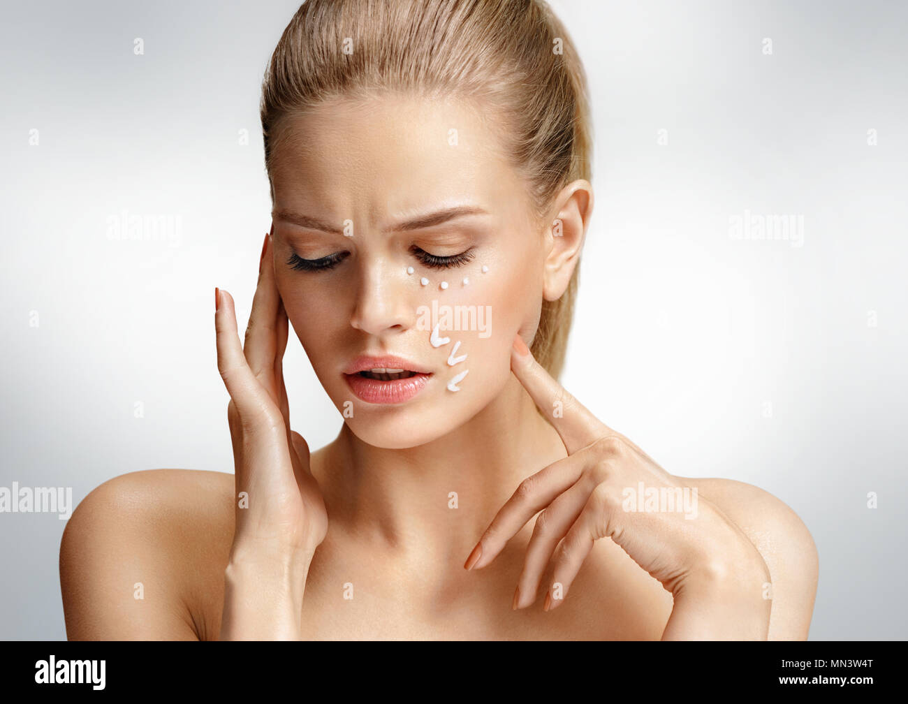 Upset woman touching her face. Photo of attractive woman with anti aging cream on grey background. Beauty & Skin care concept Stock Photo