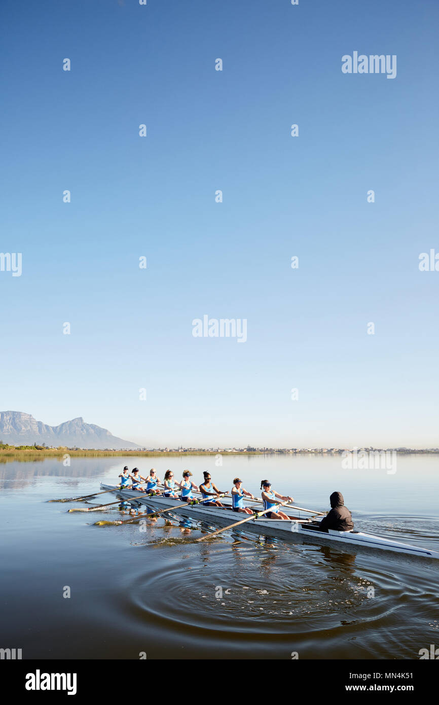 Female rowers rowing scull on tranquil lake under blue sky Stock Photo