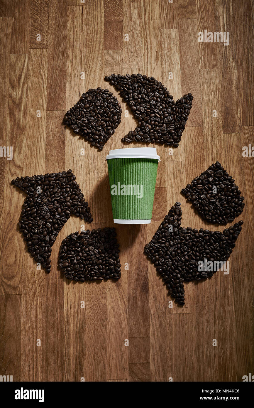 Coffee beans forming recycle symbol around green recyclable coffee cup