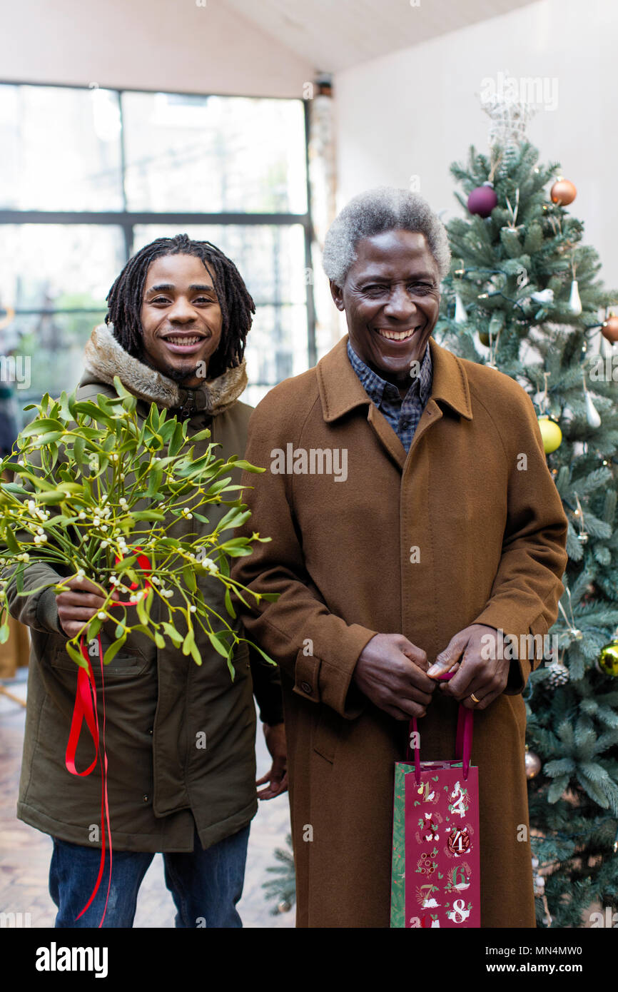 Portrait smiling grandfather and grandson arriving with Christmas gift and mistletoe Stock Photo