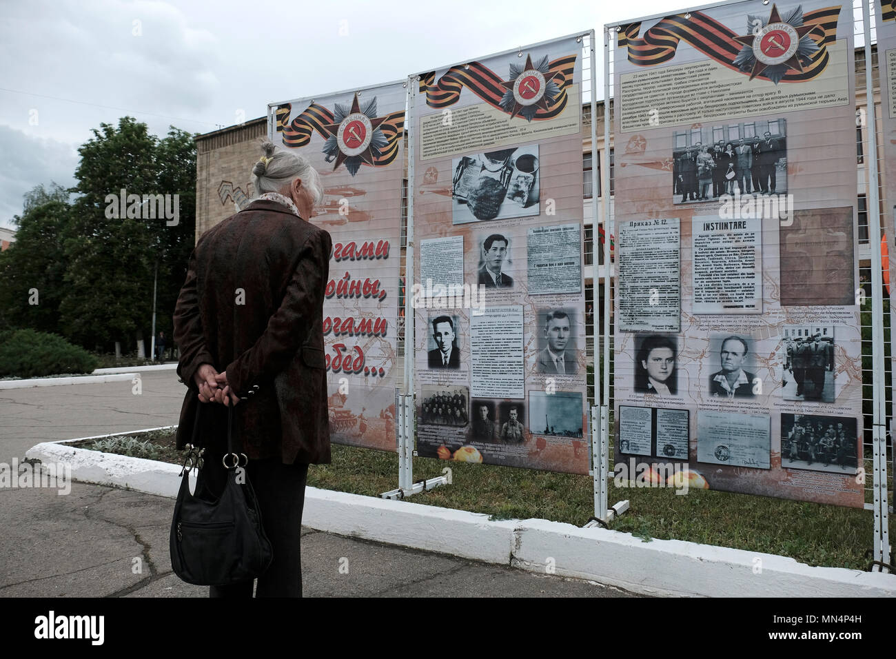 An elderly Transnistrian woman stands next to stands with old photographs of Russians who fought during World War II during the Victory Day on 9th of May which commemorates the victory of the Soviet Union over Nazi Germany in the city of Bender de facto official name Bendery within the internationally recognized borders of Moldova under de facto control of the unrecognized Pridnestrovian Moldavian Republic also called Transnistria (PMR) since 1992. Stock Photo