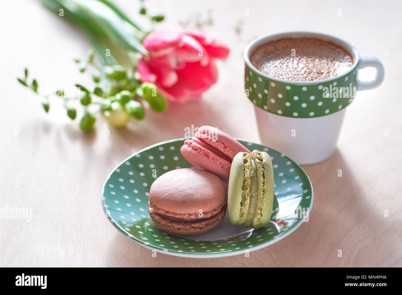 Spring coffee background. Pink tulip, freesia, espresso and macarons in front, spring flowers in