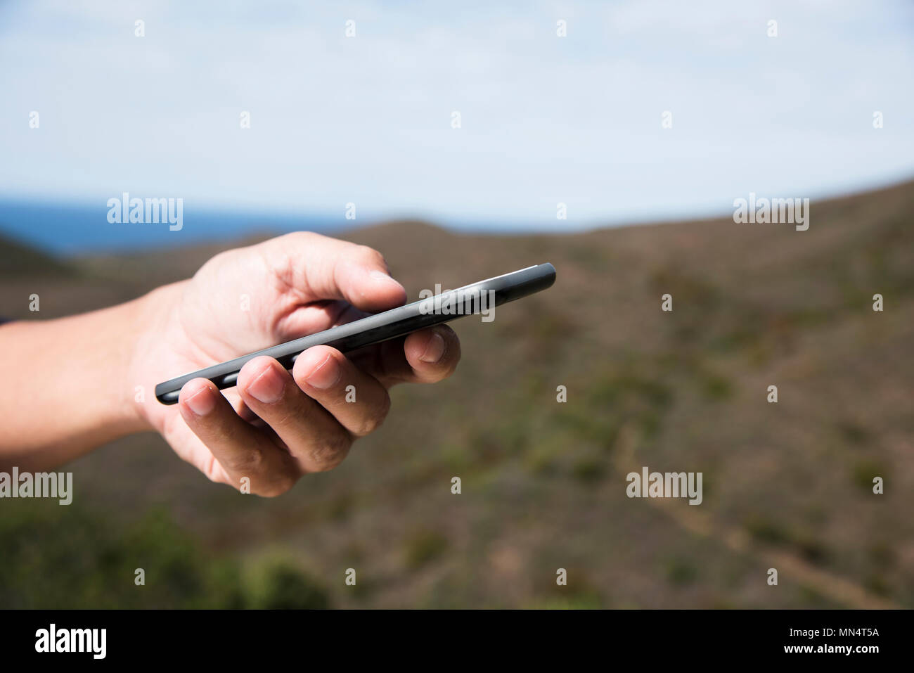 closeup of a young caucasian man using a smartphone outdoors, in the mountains Stock Photo