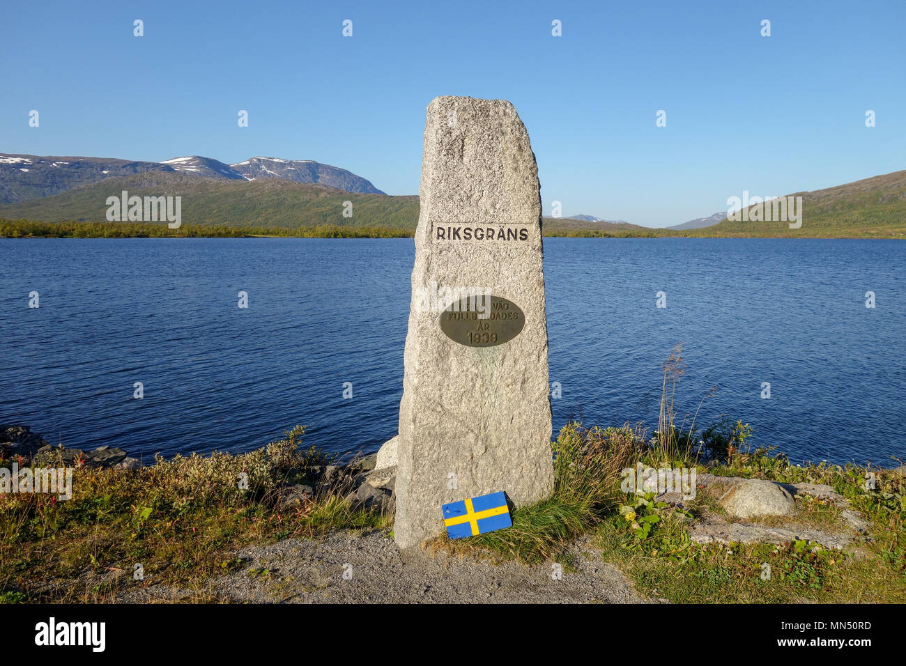 Summer day. Stone marking the border crossing between Sweden and Norway at E12 road to Mo I Rana. Road was made 1939. Umbukta lake in the back. Stock Photo