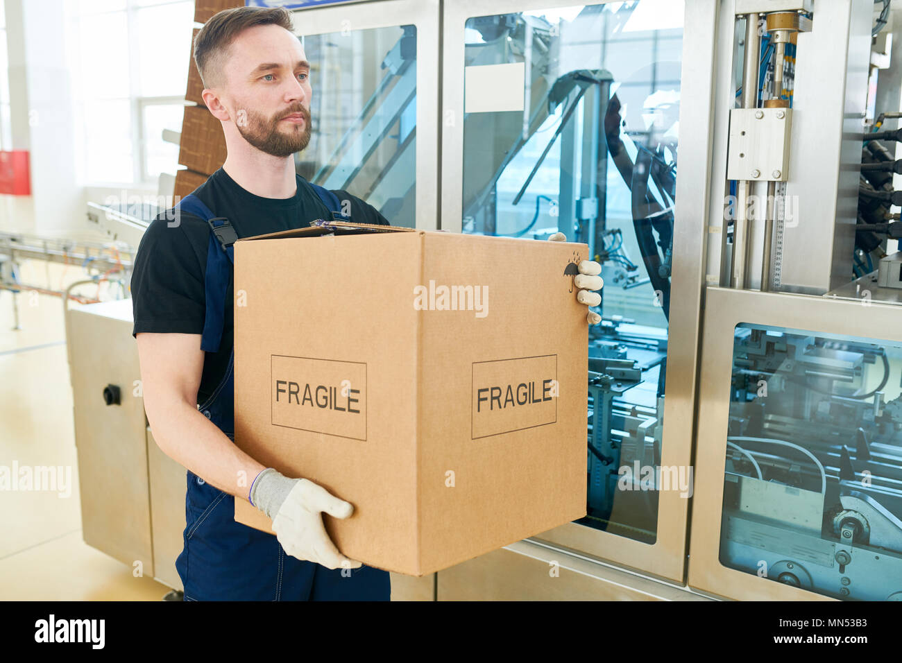 https://c8.alamy.com/comp/MN53B3/portrait-shot-of-confident-worker-wearing-overall-and-handling-gloves-carrying-cardboard-box-and-walking-along-spacious-dairy-factory-warehouse-MN53B3.jpg