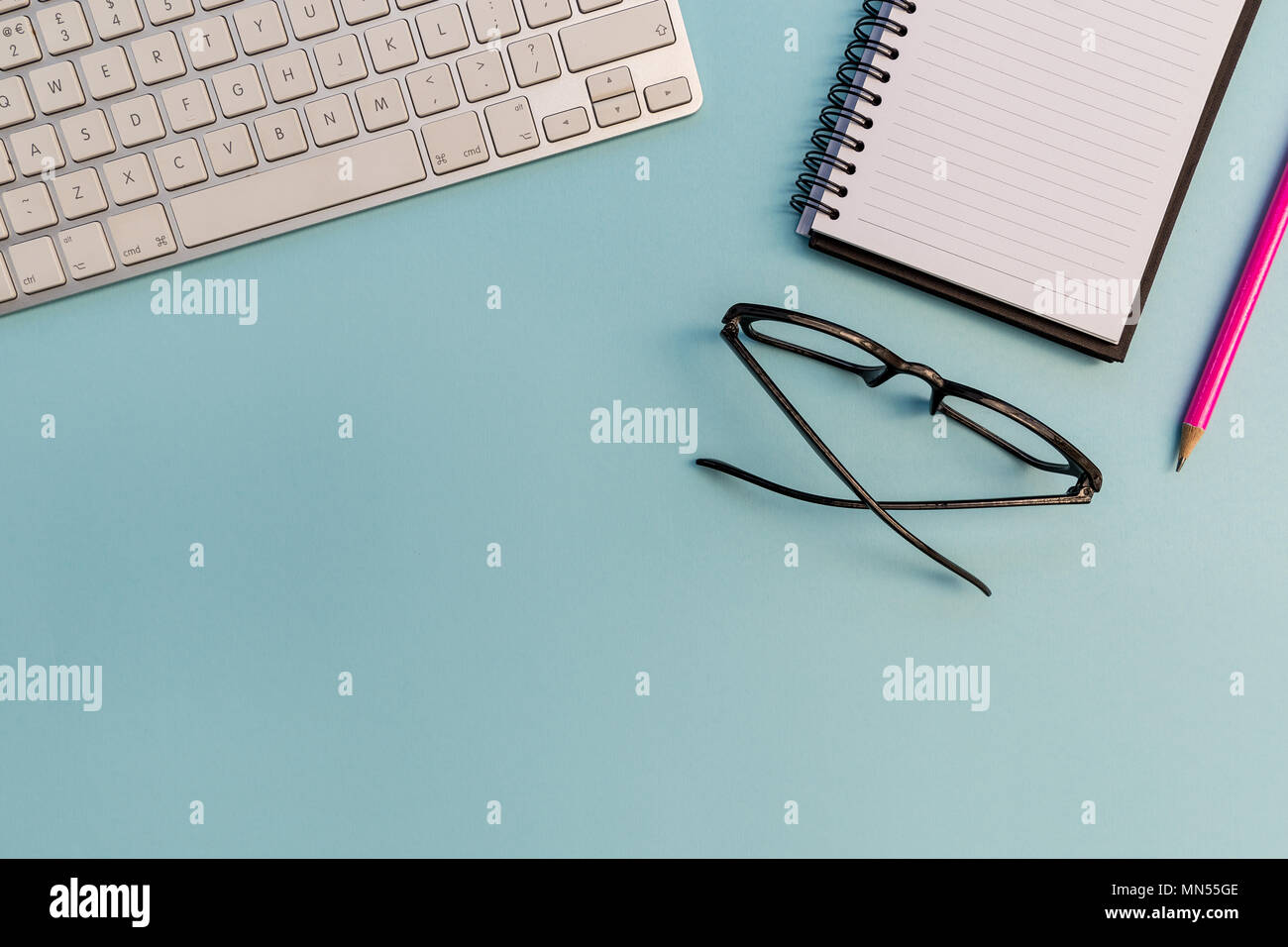 Computer keyboard notebook pencil and eyeglasses on bright blue background Stock Photo