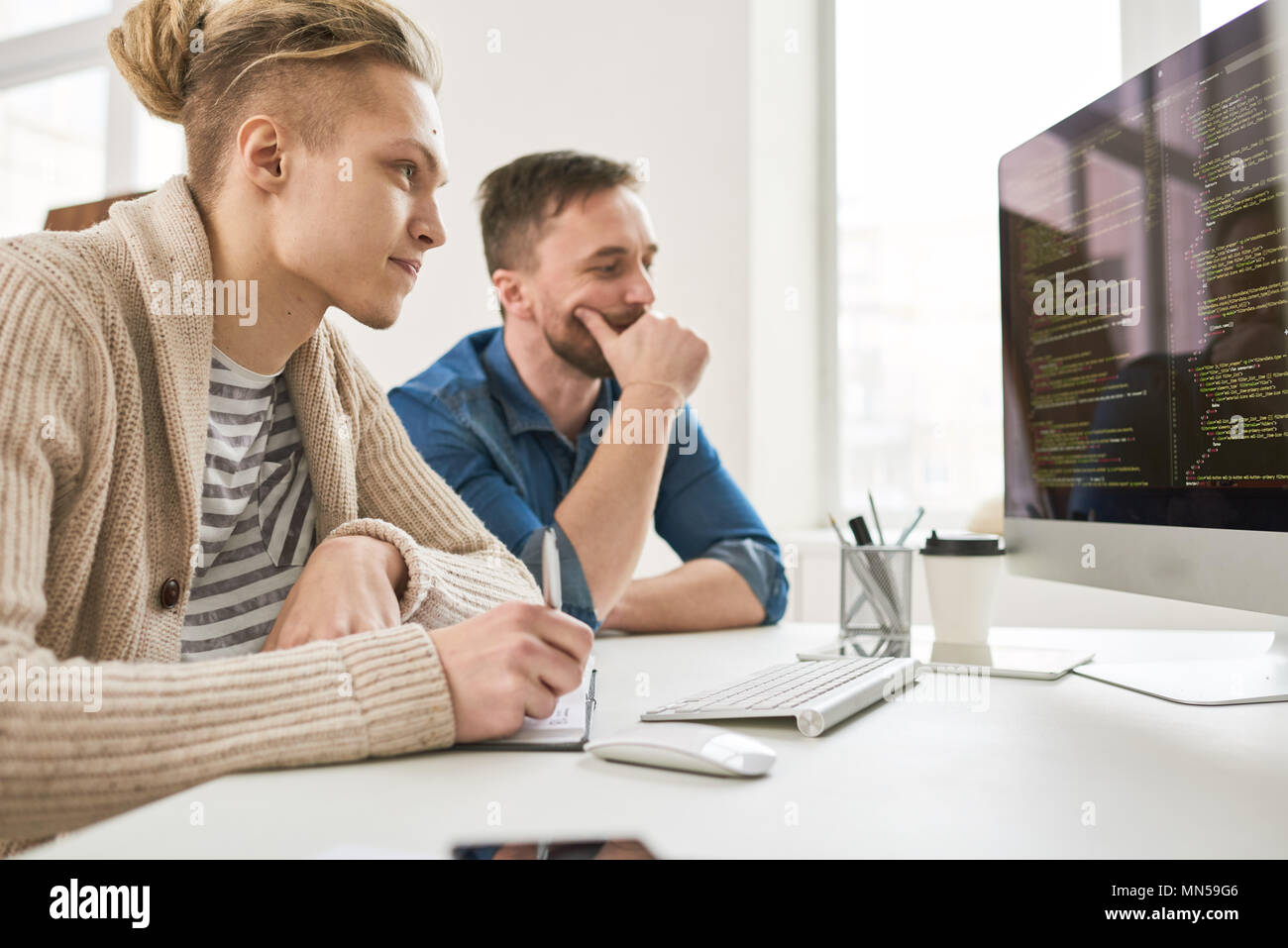 Side view portrait of two contemporary program developers writing code sitting at desk using computer and collaborating on startup project in modern o Stock Photo