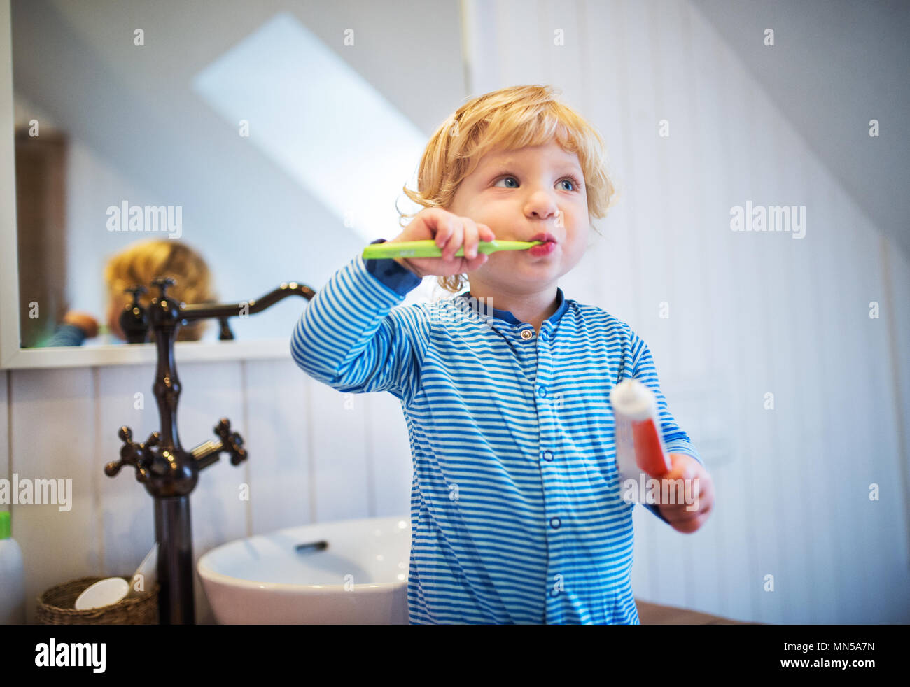 Cute toddler brushing his teeth in the bathroom. Little boy standing on a stool. Stock Photo