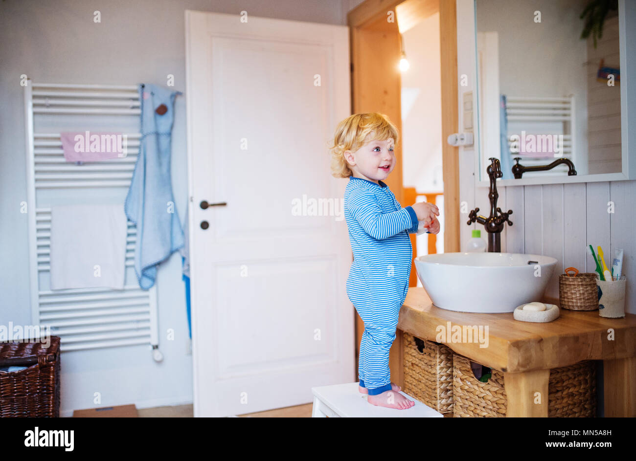 Cute toddler boy standing on a stool in front of mirror in the bathroom