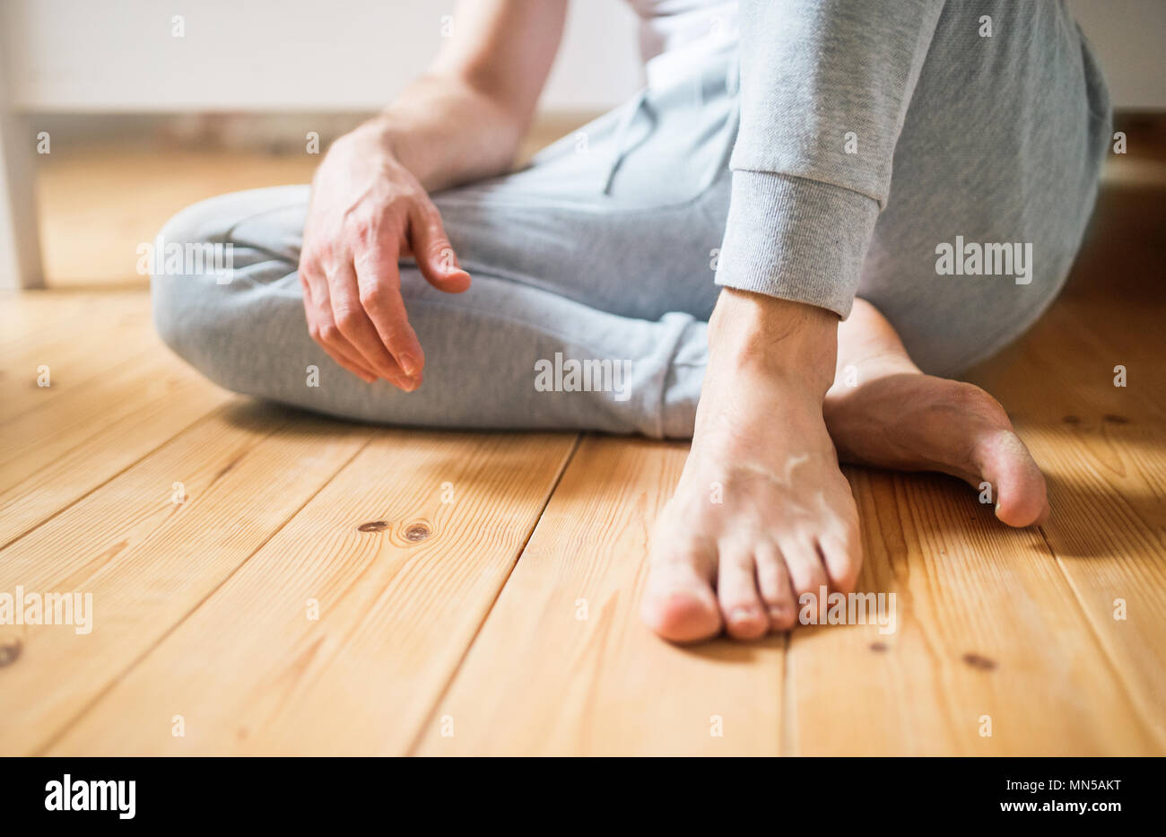 Unrecognizable barefoot man sitting on the floor in bedroom at home