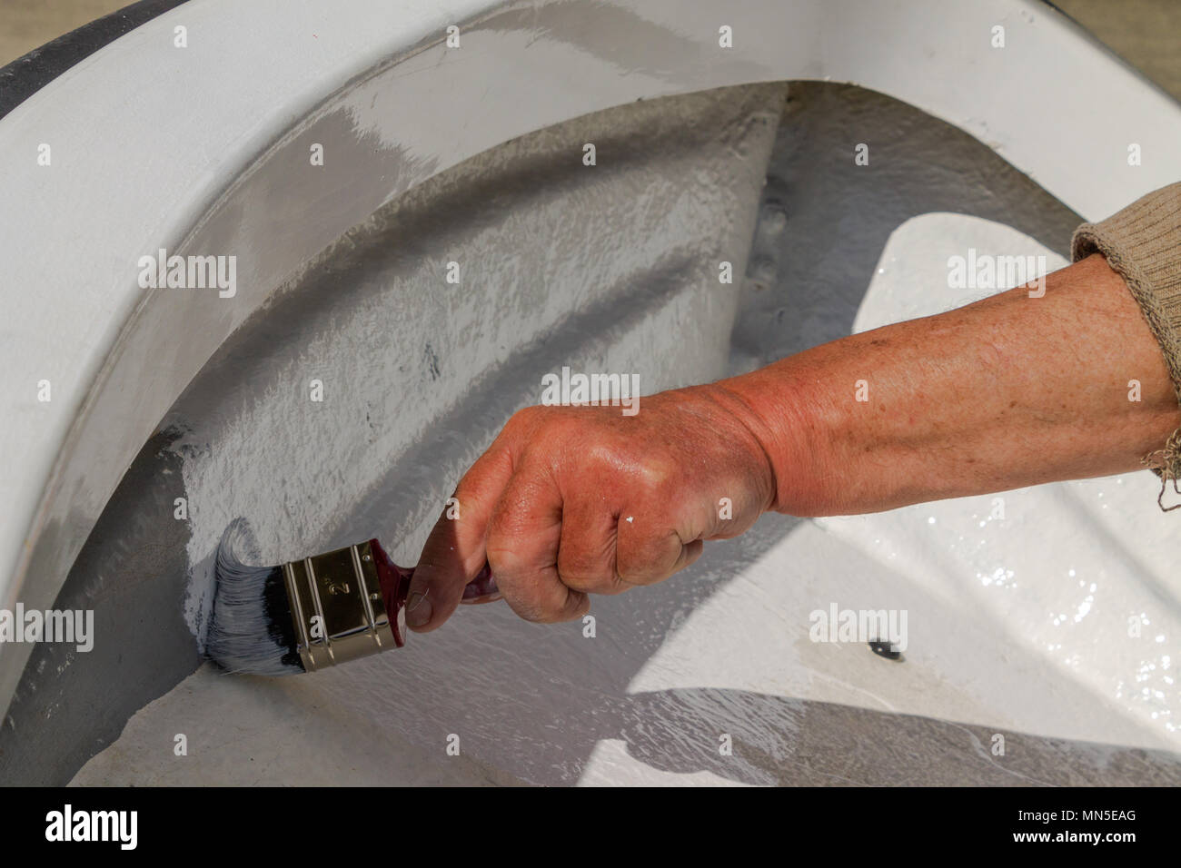 close up of painting the top coat of white paint onto the fibreglass hull of a fibreglass boat, using marine gloss paint. Stock Photo