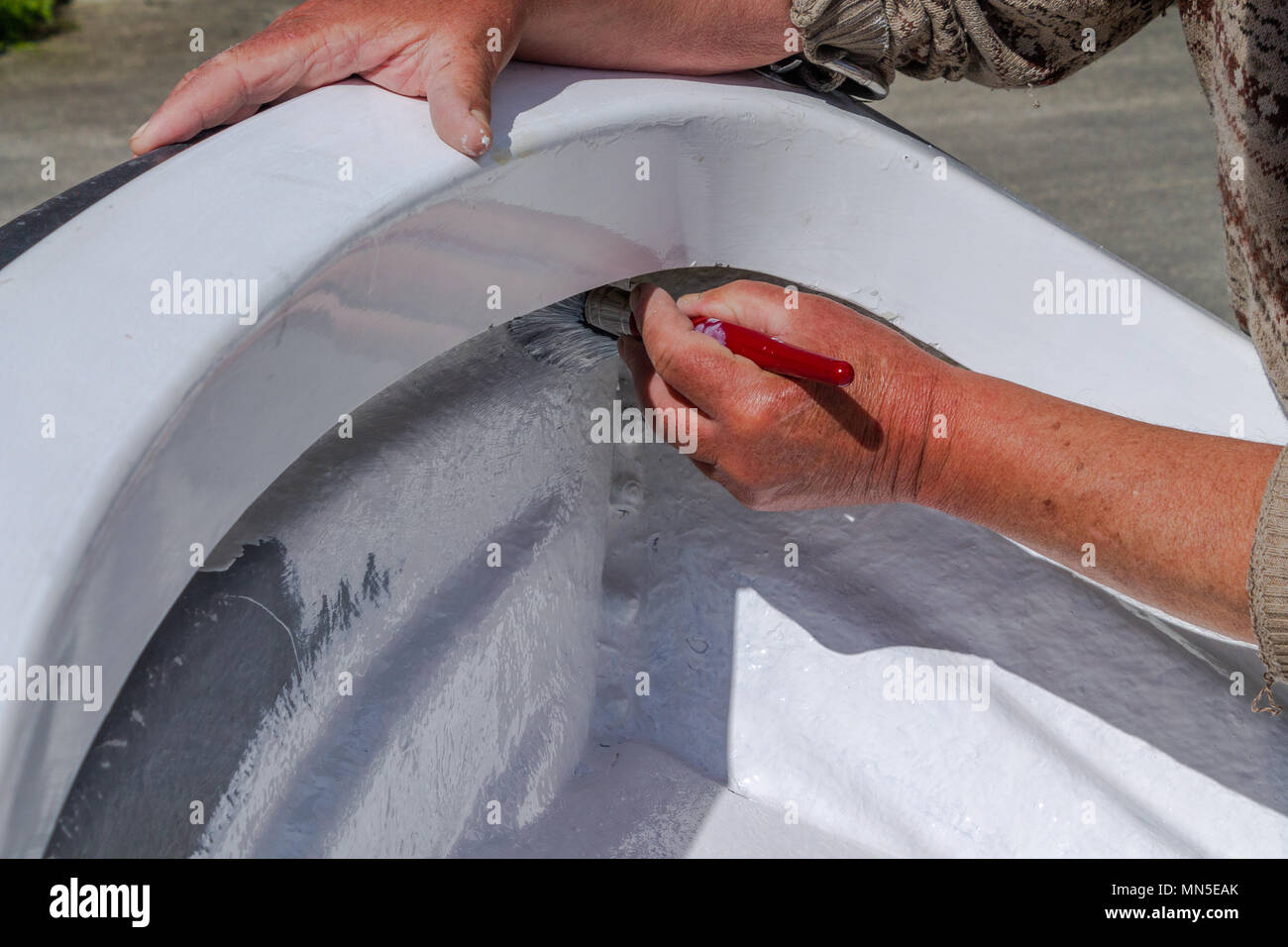 close up of painting the top coat of white paint onto the fibreglass hull of a fibreglass boat, using marine gloss paint. Stock Photo