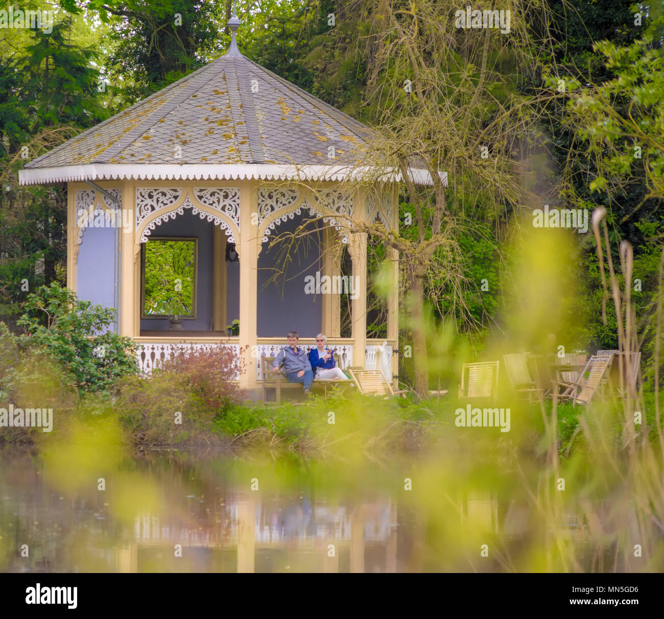 Celle, Lower Saxony, Germany, April 28, 2018: A couple sitting on a bench in front of an old-fashioned little pavilion in a public garden, intensional Stock Photo