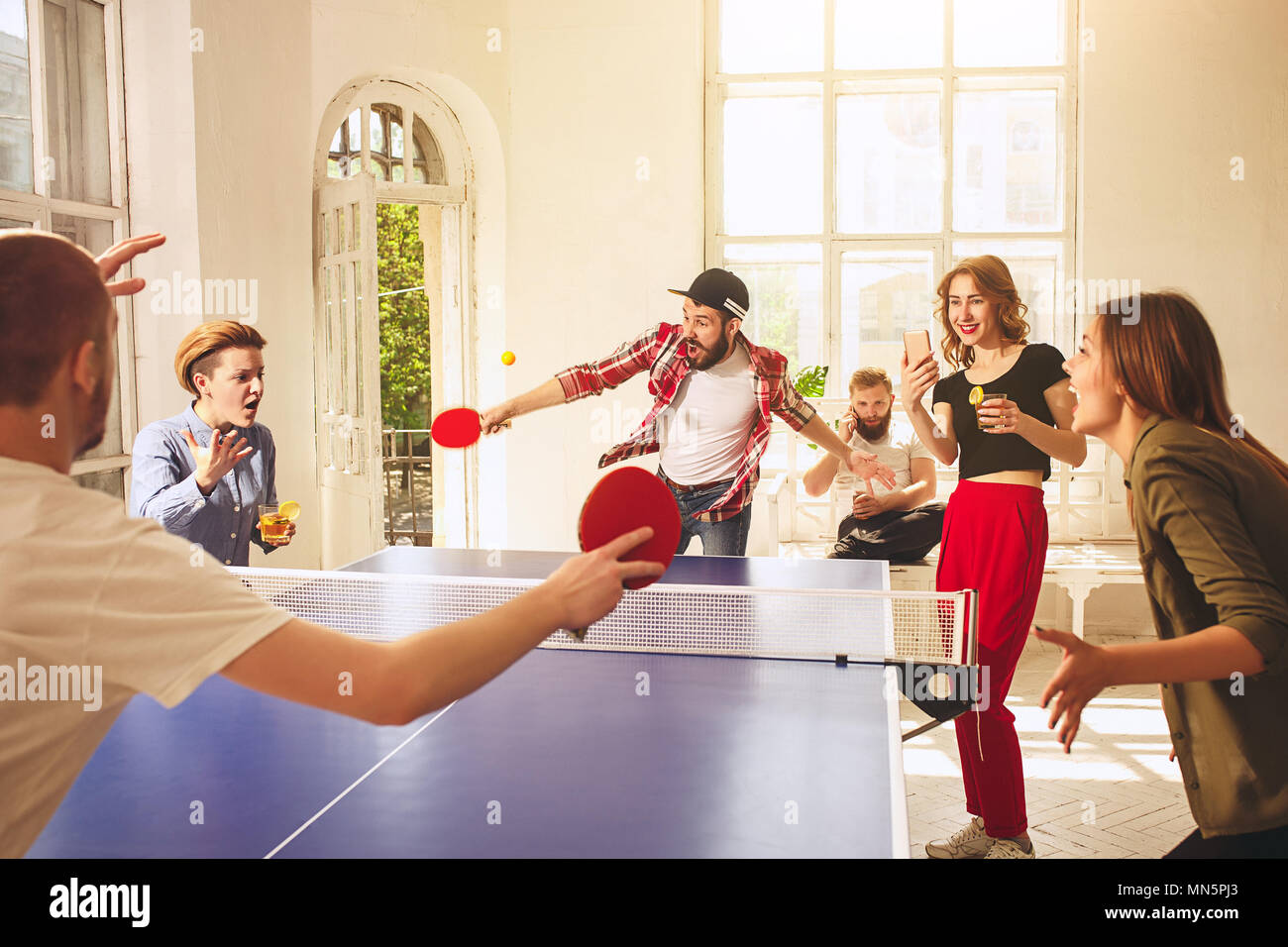 Group of happy young friends playing ping pong table tennis Stock Photo