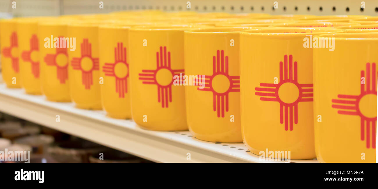 Colorful souvenir mugs featuring the New Mexican State Flag - a red sun petroglyph against a yellow background. Stock Photo