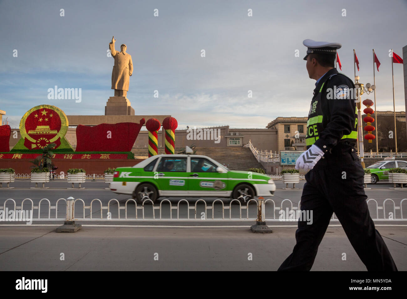 A Chinese policeman walks down the street past a huge monument to Mao Zedong in Kashgar city, Xinjiang Uygur Autonomous Region of China Stock Photo