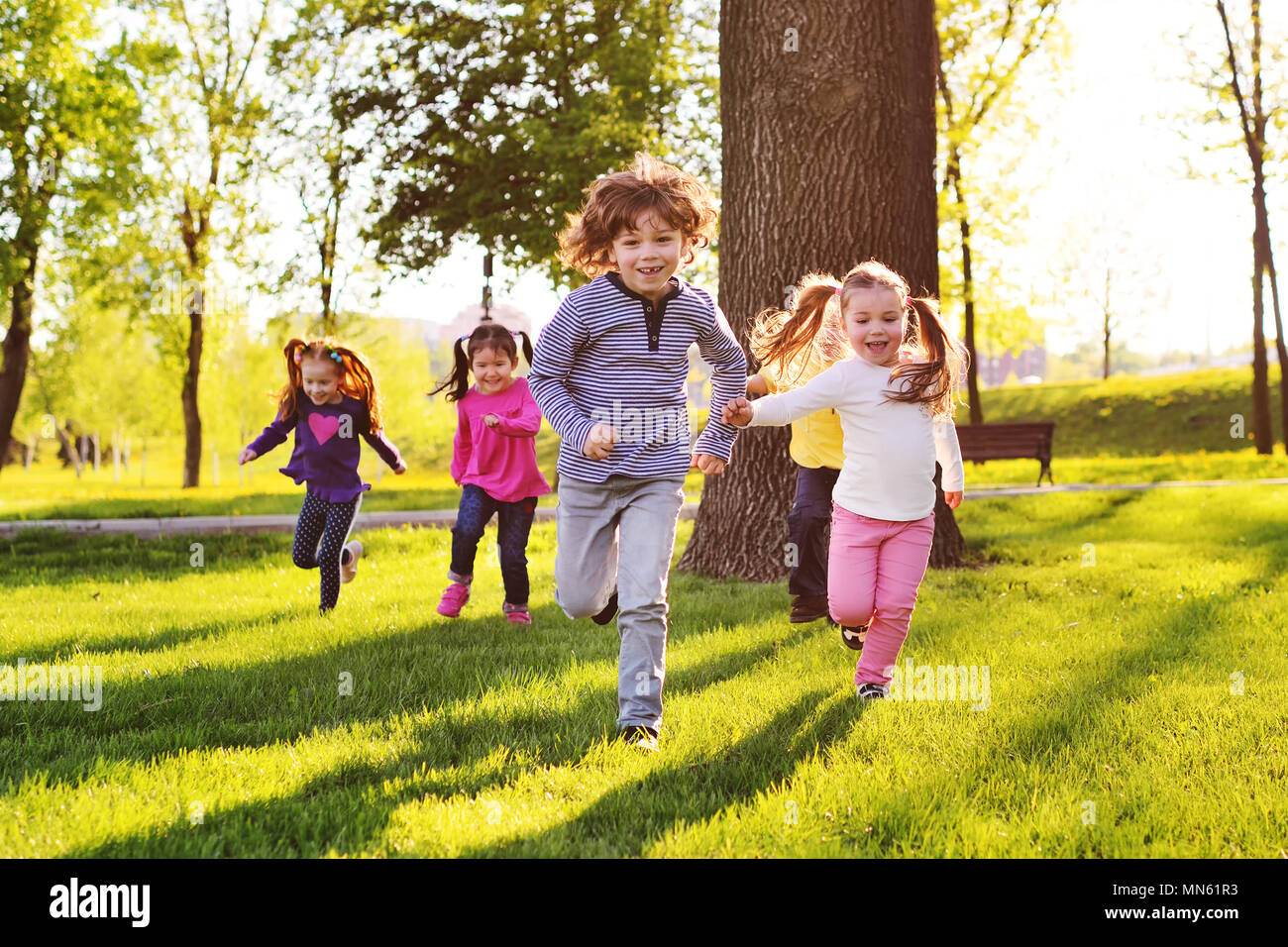 many young children smiling running along the grass in the park. Stock Photo