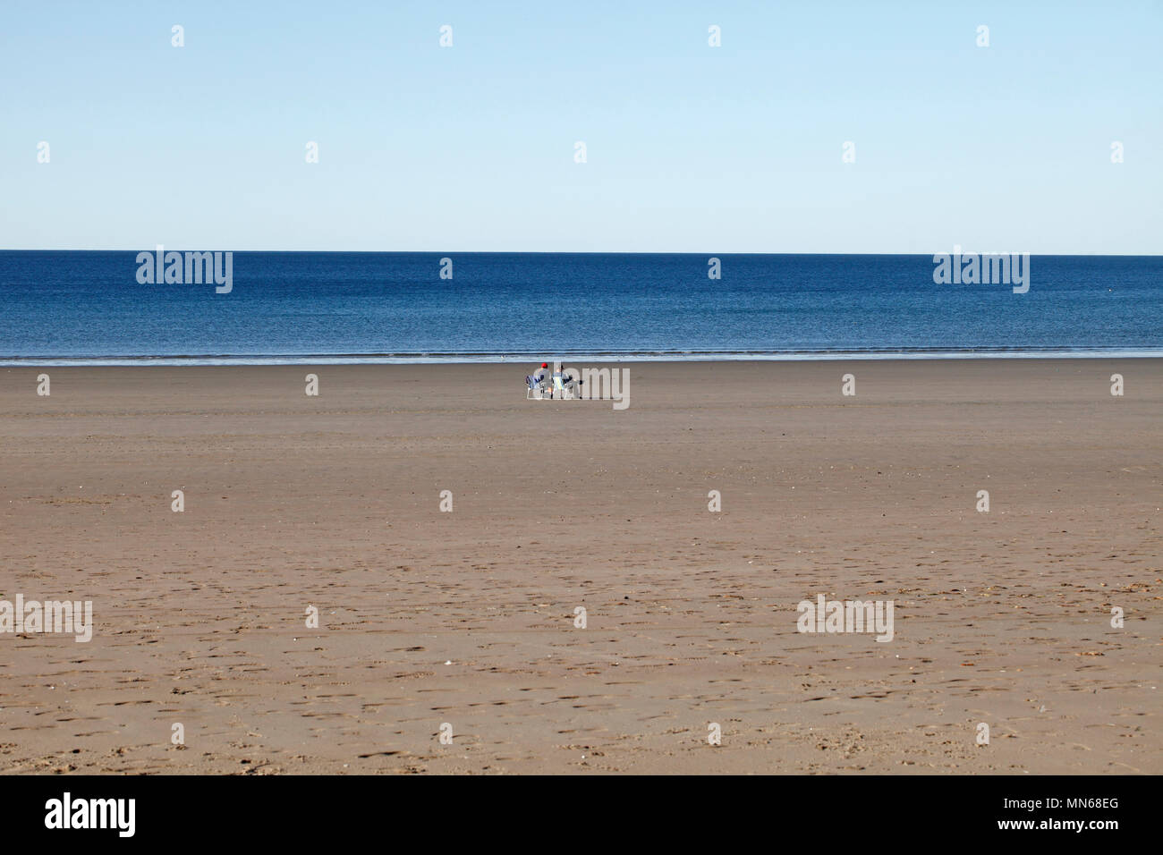 Two people in deckchairs on a Wide open empty beach at Puerto Madryn, Chubut Province, Argentina. Stock Photo