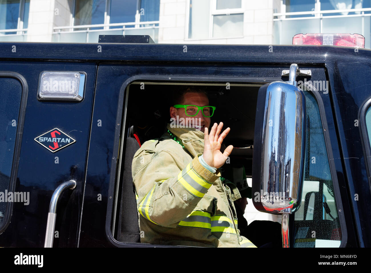 A fireman wearing bright green glasses waving to the crowd in the Montreal St Patricks Day parade Stock Photo