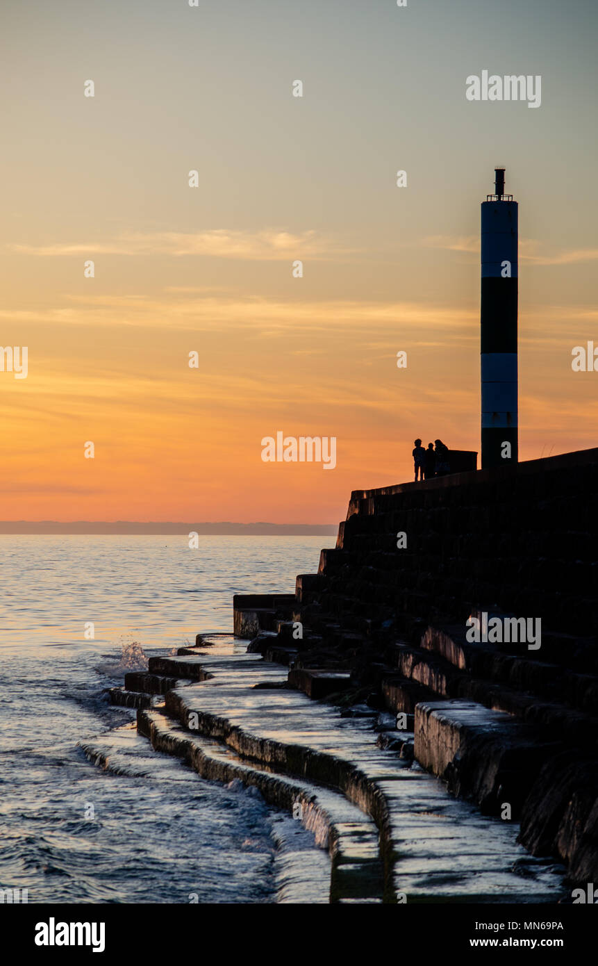 Aberystwyth Sunset at the lighthouse. A group of people stand at the end looking over the water and gazing at the sunset. Stock Photo