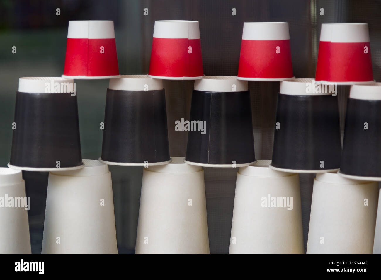 Disposable paper cups in the cafe showcase. Coffee to go. Red, black and white ecological cups of different sizes and shapes pyramid upside down behin Stock Photo