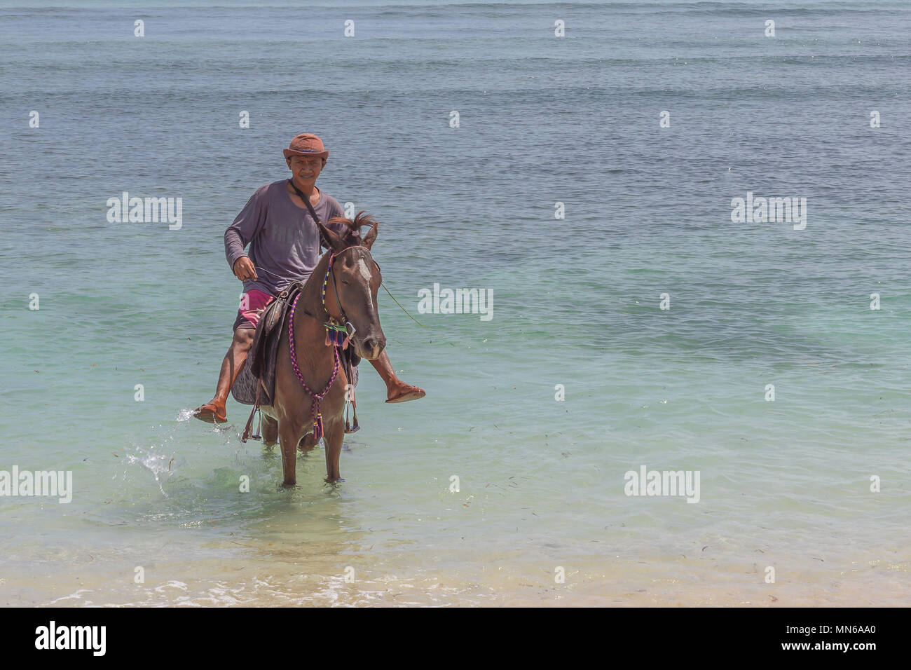A man riding his horse in the shallow blue and green tropical  water at  Gili Trawangan, Indonesia, april 24, 2018, Stock Photo