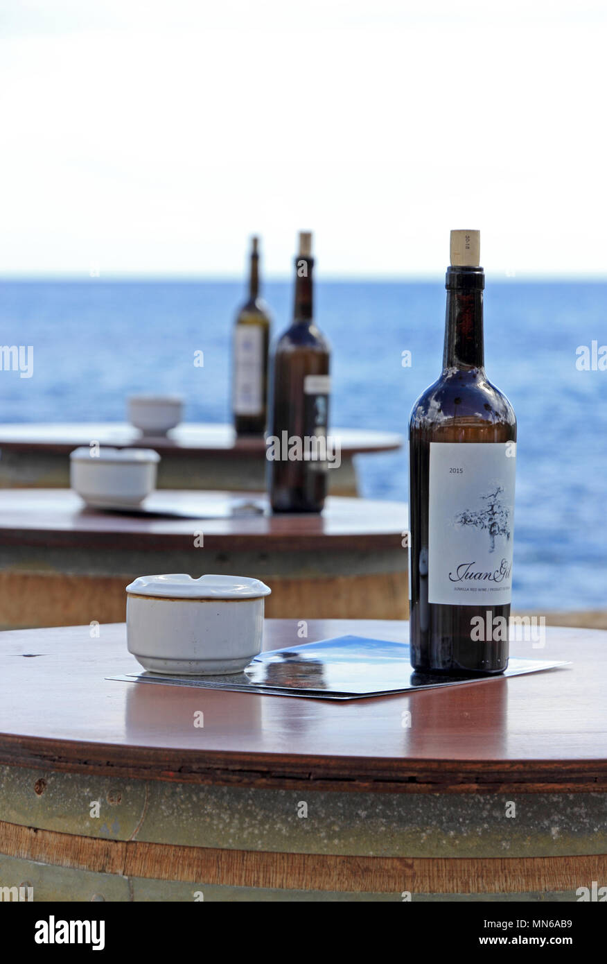 Barrels support table top with ashtrays and wine bottles outside seafront bar, Cala Bona, Mallorca Stock Photo