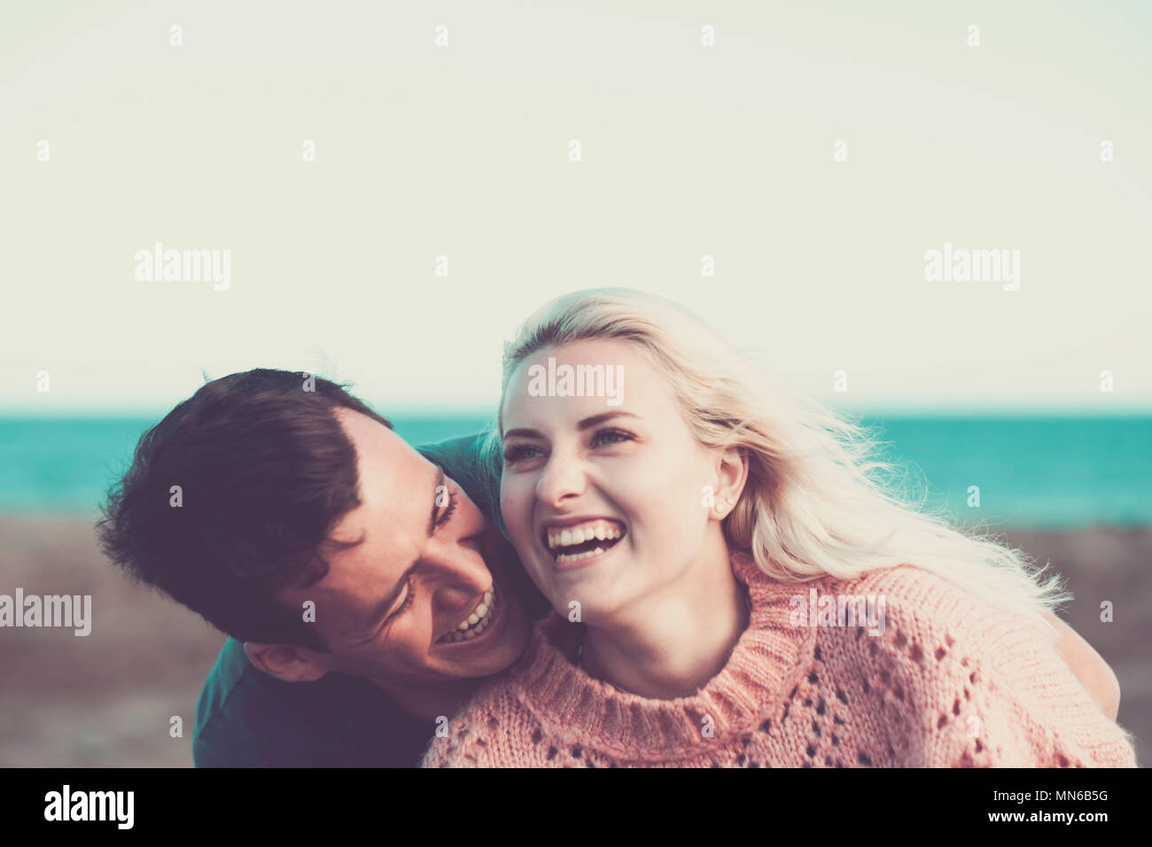 young caucasian couple blonde and black hair stay together with joy and love outdoor with beach and ocean in background. leisure vacation concept with Stock Photo