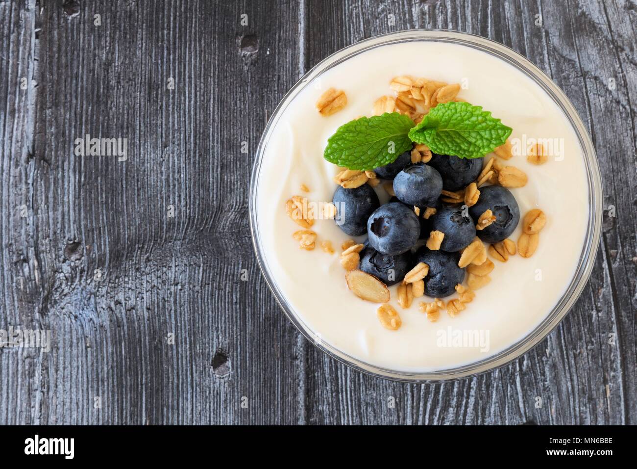 Bowl of yogurt with blueberries and granola, above view on rustic dark wood Stock Photo