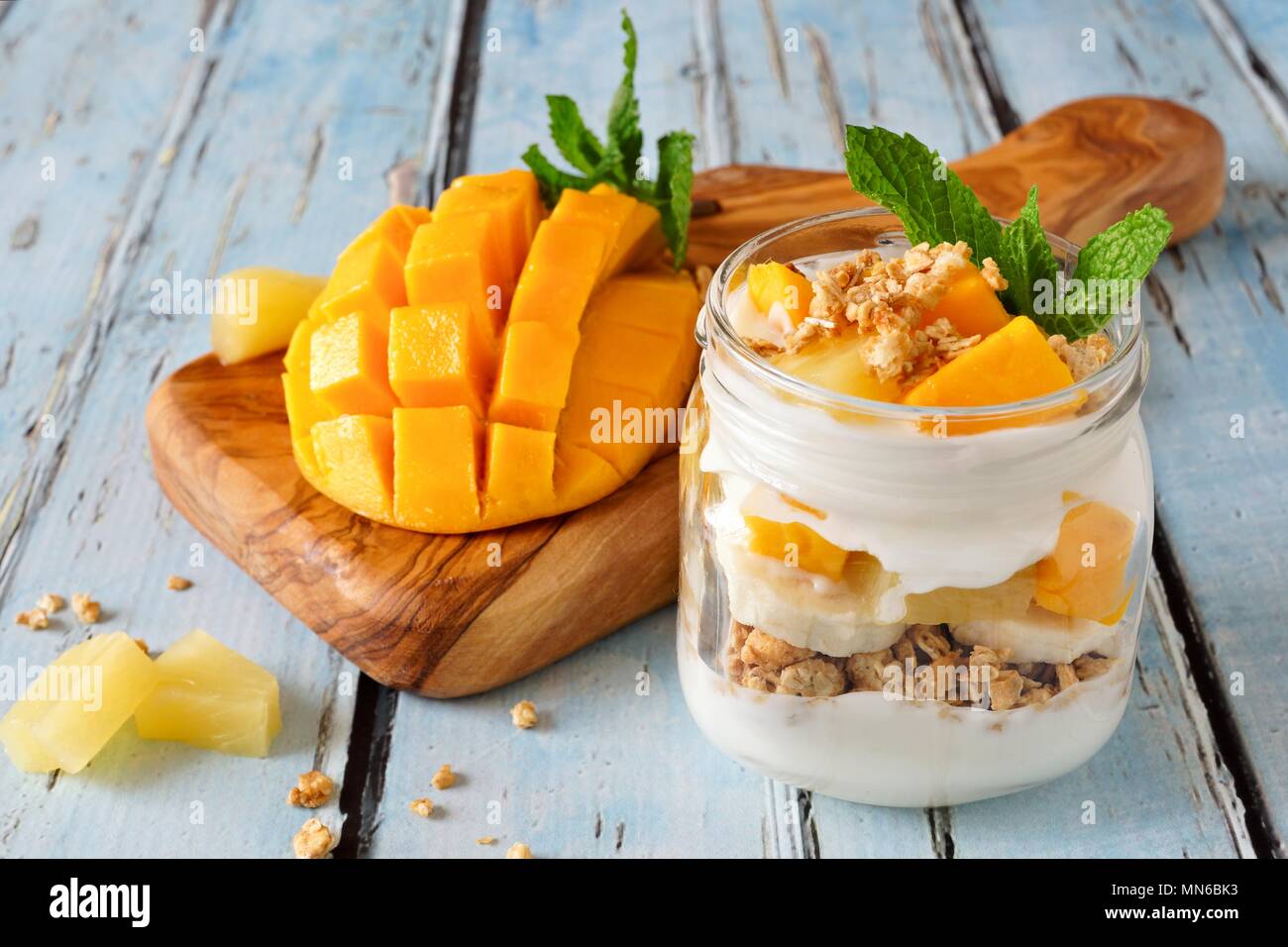 Tropical mango and pineapple parfait in a mason jar on a rustic blue wood background Stock Photo