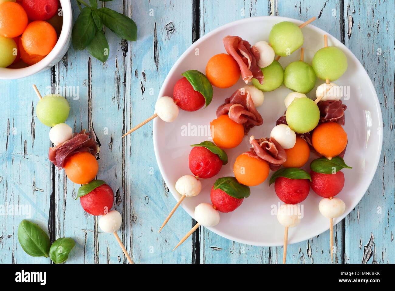 Plate of delicious summer fruit skewers with melon, cheese and prosciutto on a rustic blue wood