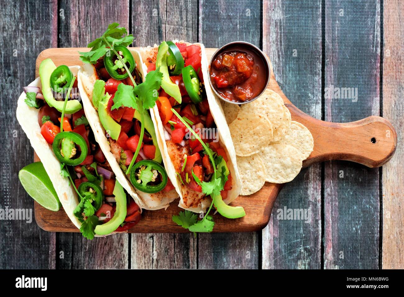 Spicy fish tacos with watermelon salsa and avocados on a paddle board against a rustic wood background Stock Photo