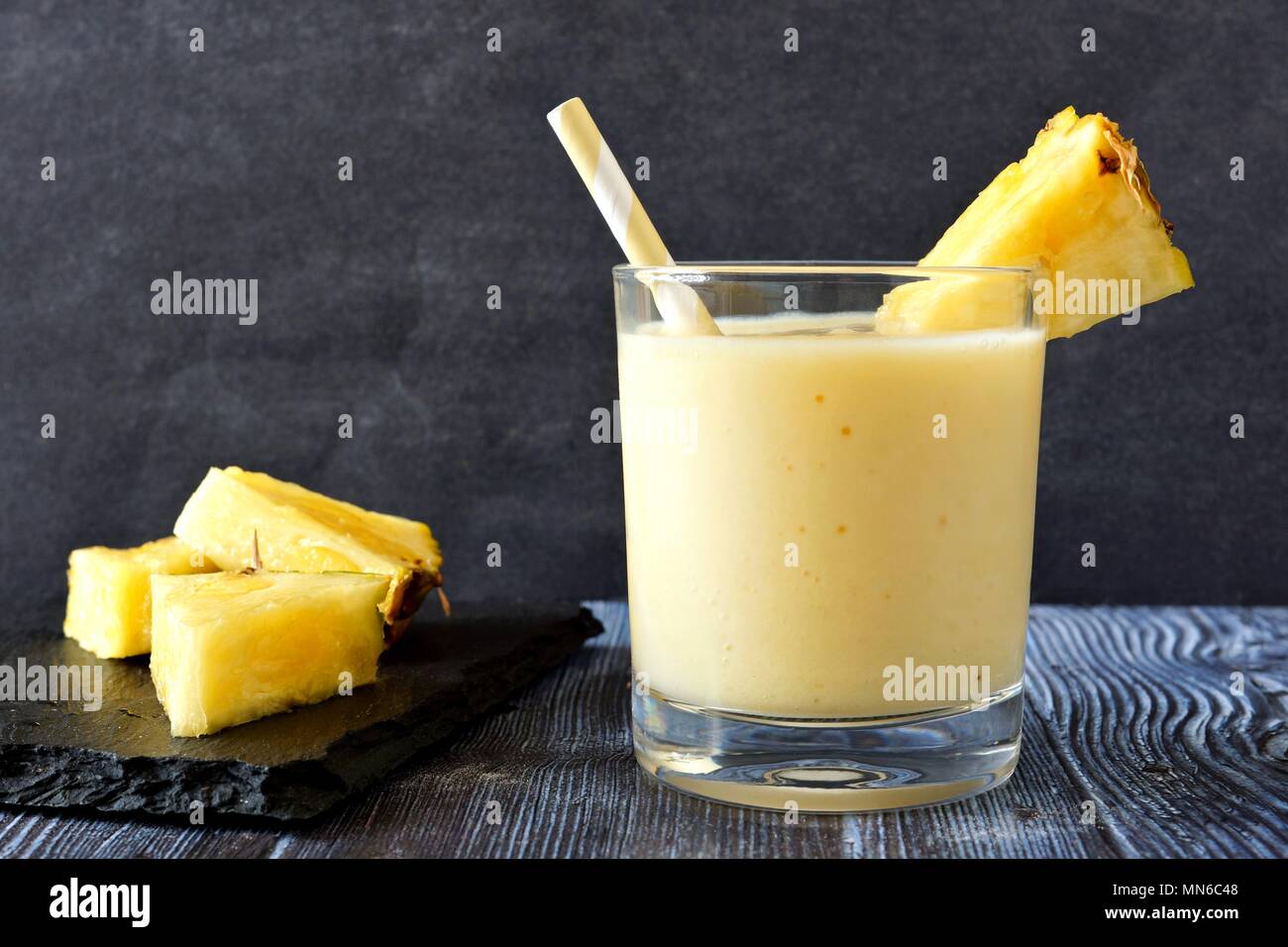 Healthy pineapple smoothie in a glass with straw against a dark background Stock Photo