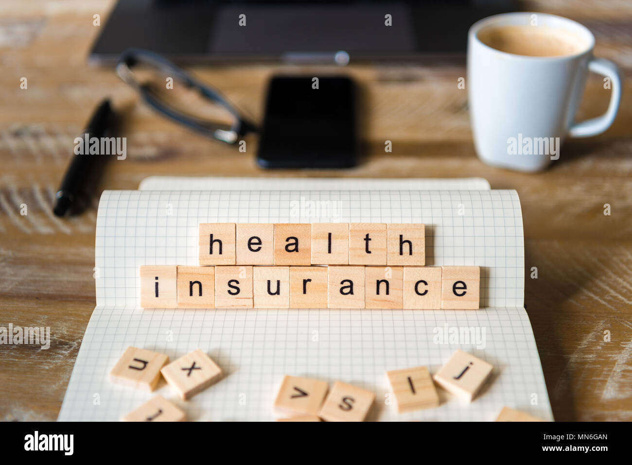 Closeup on notebook over wood table background, focus on wooden blocks with letters making Health Insurance words. Stock Photo