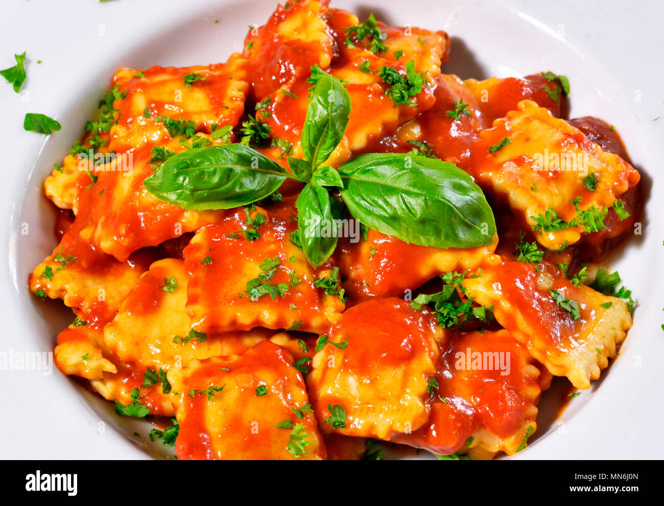 Fresh ravioli pasta with parsley and basil leaf, italian cuisine. White plate and wooden table, pasta dish. Stock Photo