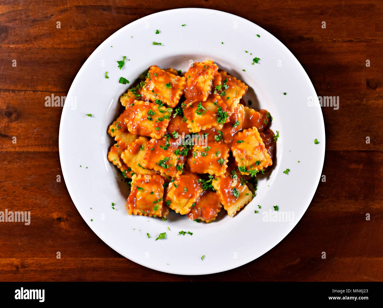 Fresh ravioli pasta with parsley and basil leaf, italian cuisine. White plate and wooden table, pasta dish. Stock Photo