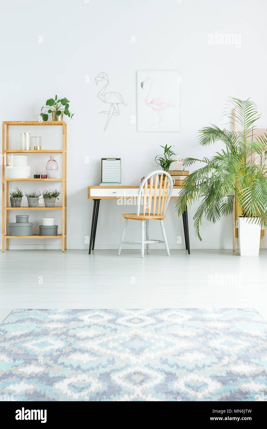 Chair at desk between plant and shelves in bright workspace with patterned carpet and poster Stock Photo