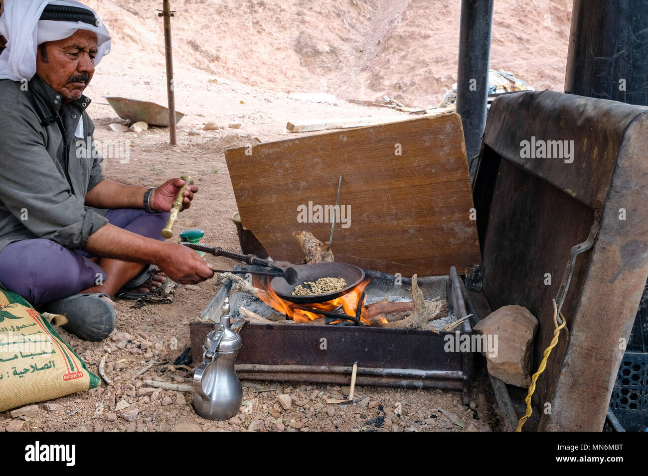 A bedouin sits on the ground and roast beans on fire to prepare traditional coffee Stock Photo