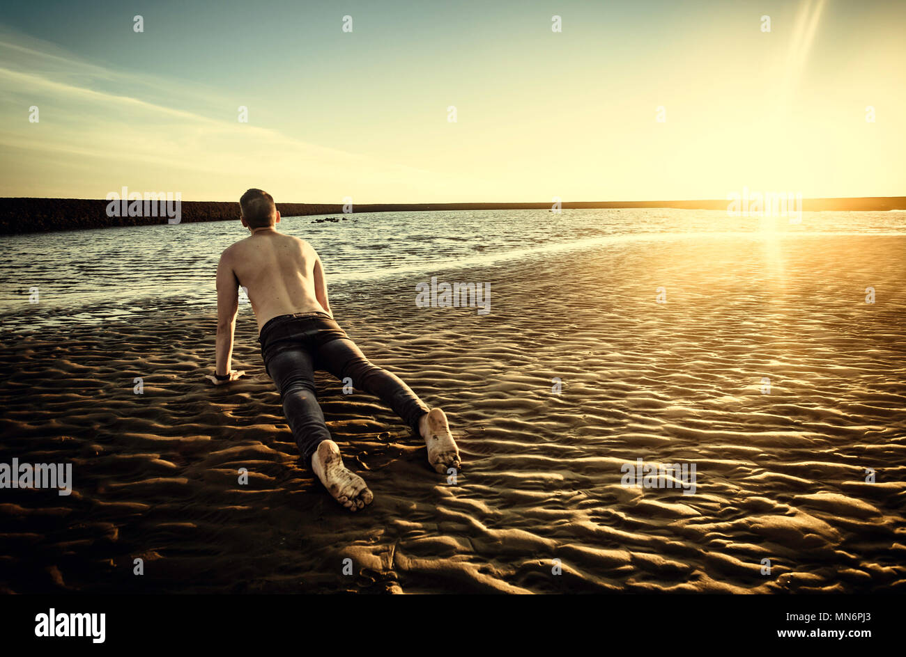 Young man doing yoga in the sand of the beach of Sanlucar de Barrameda at sunset, when the tide is low Stock Photo