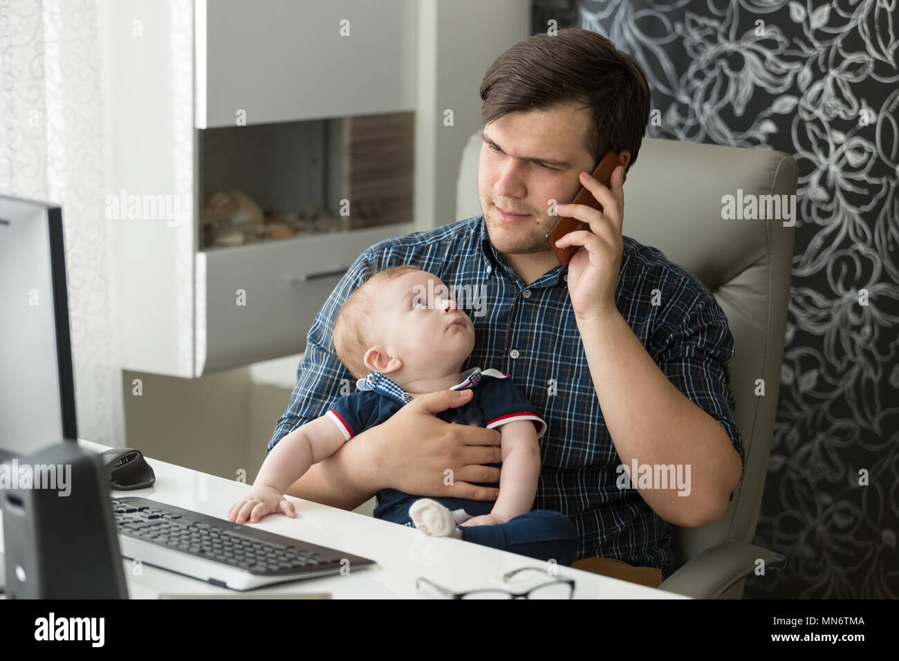 Portrait of young busy man working at home office and looking after his bbay son Stock Photo