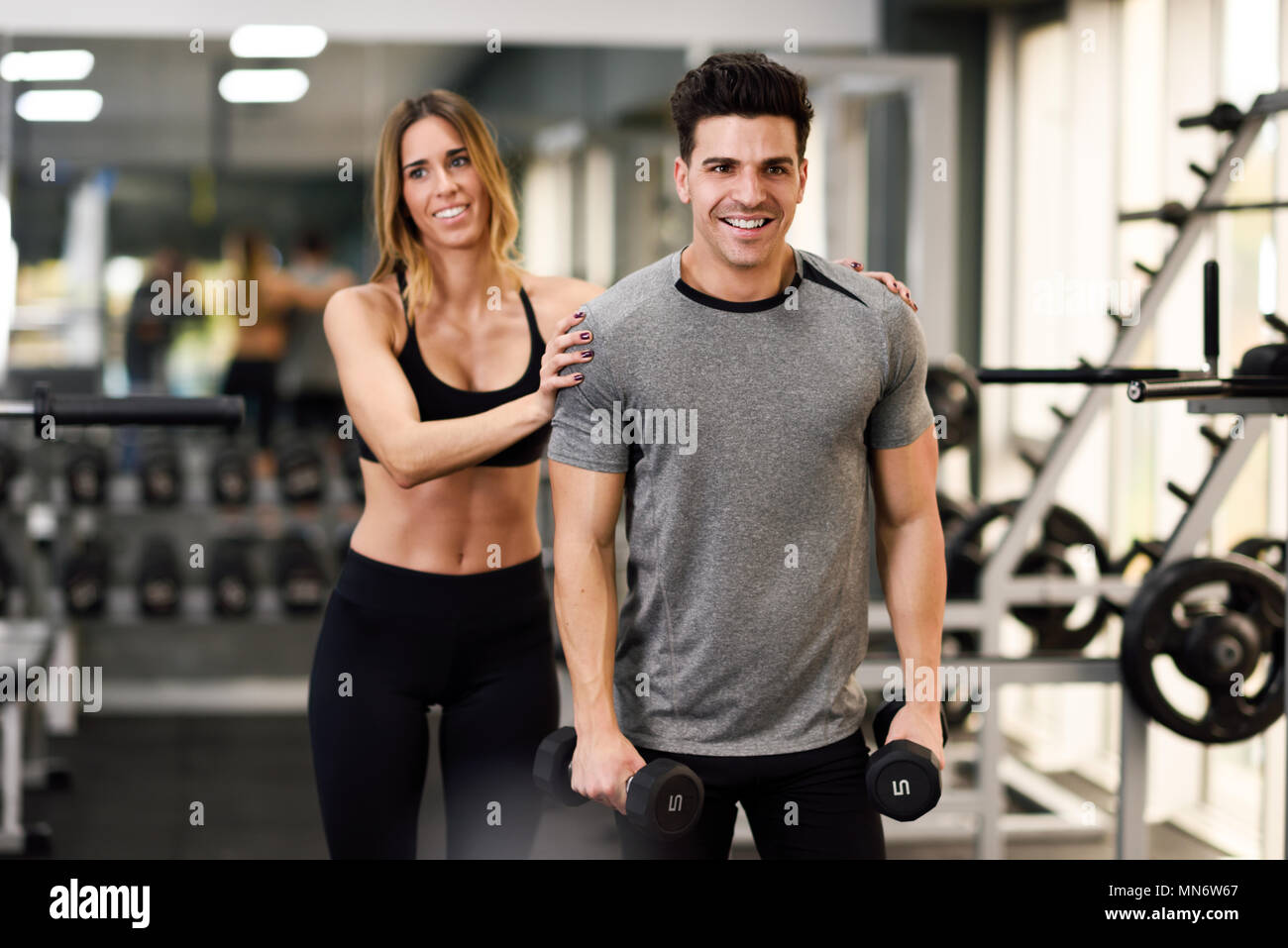 Female personal trainer helping a young man lift dumbells while