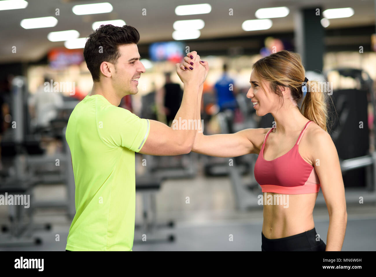 Smiling young man and woman doing high five in gym. Couple wearing sportswear Stock Photo
