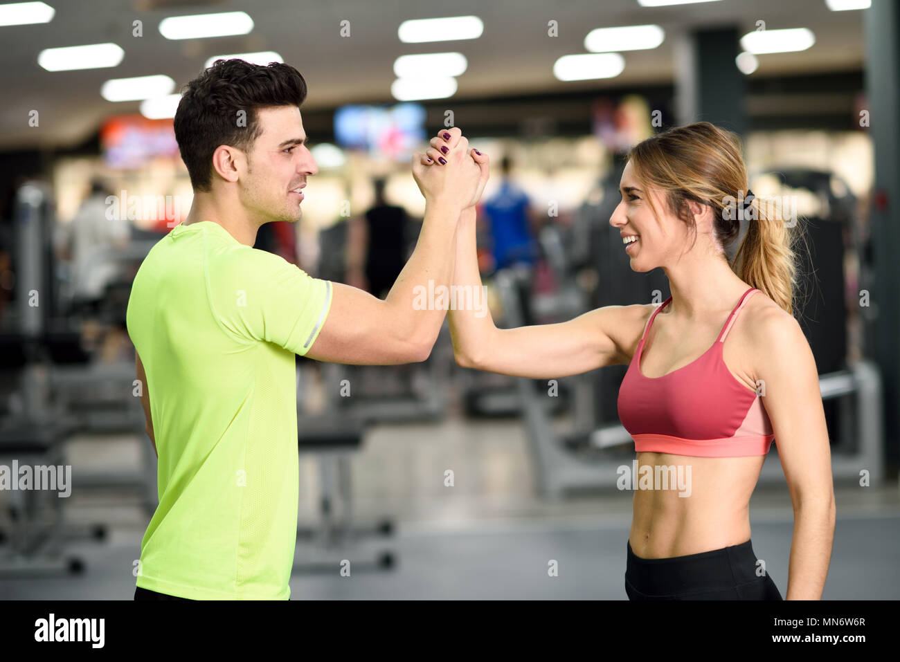 Smiling young man and woman doing high five in gym. Couple wearing sportswear Stock Photo