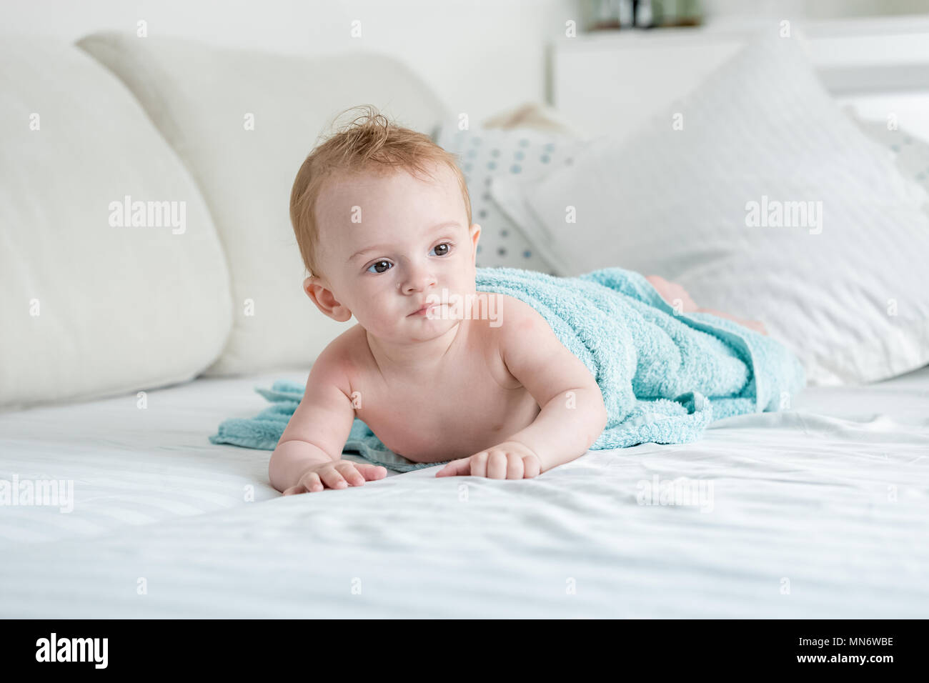 Adorable 9 months old baby boy lying on bed under big blue towel after